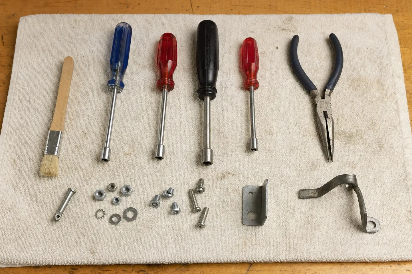 Nut drivers, pliers, a brush and loose hardware laid out in rows on a cloth over a workbench
