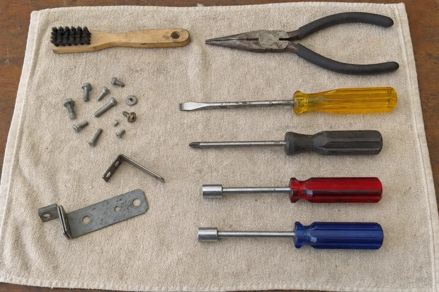 Drivers, pliers, a wire brush and a flat strike plate laid out on a towel with the screws that came off with it