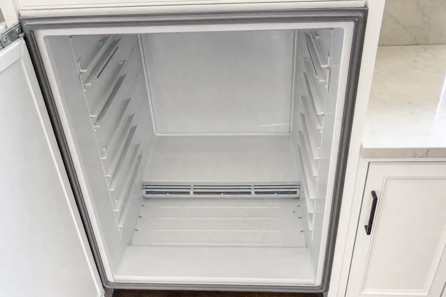 Empty refrigerator compartment with every shelf taken out and the low rear air grille exposed