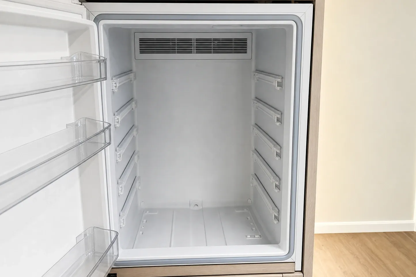 Empty freezer cavity with the door open, bare shelf ladders and a wide air grille across the back wall
